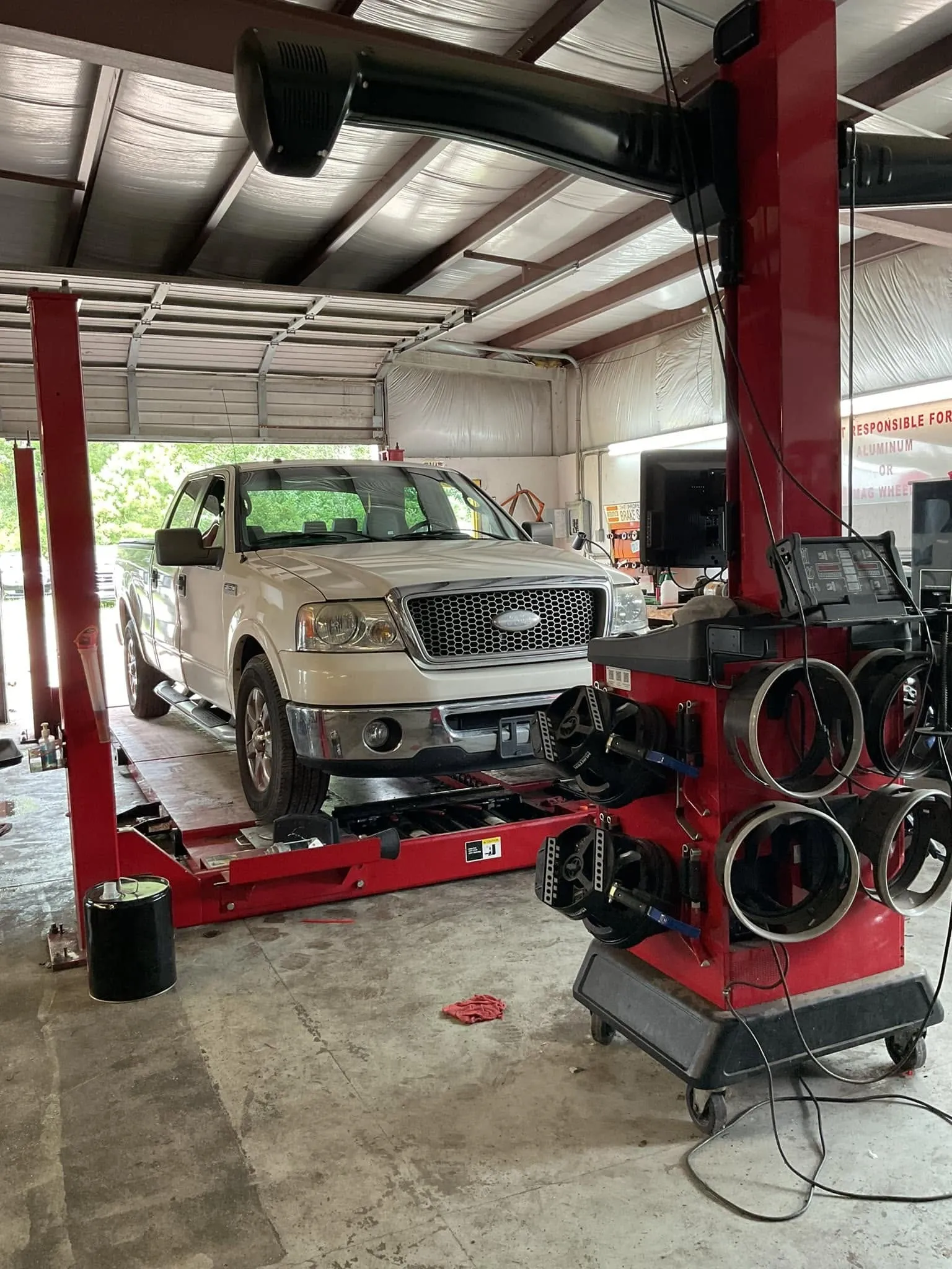A Ford F-150 up on the red alignment rack in the Riverside Automotive shop, next to the alignment machine.