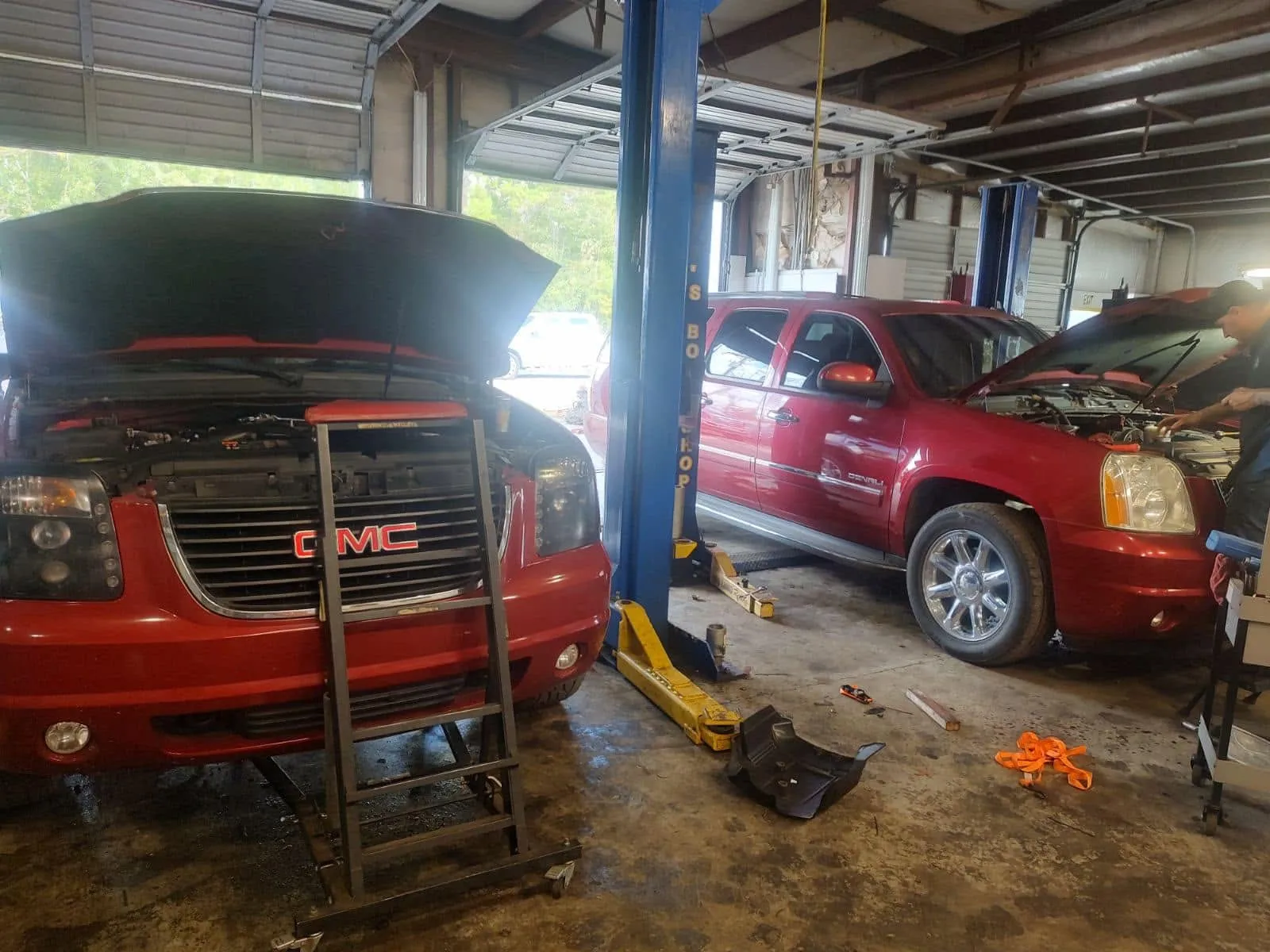 Two GMC Yukon SUVs in the Riverside Automotive bays with hoods up during engine and cooling-system work.
