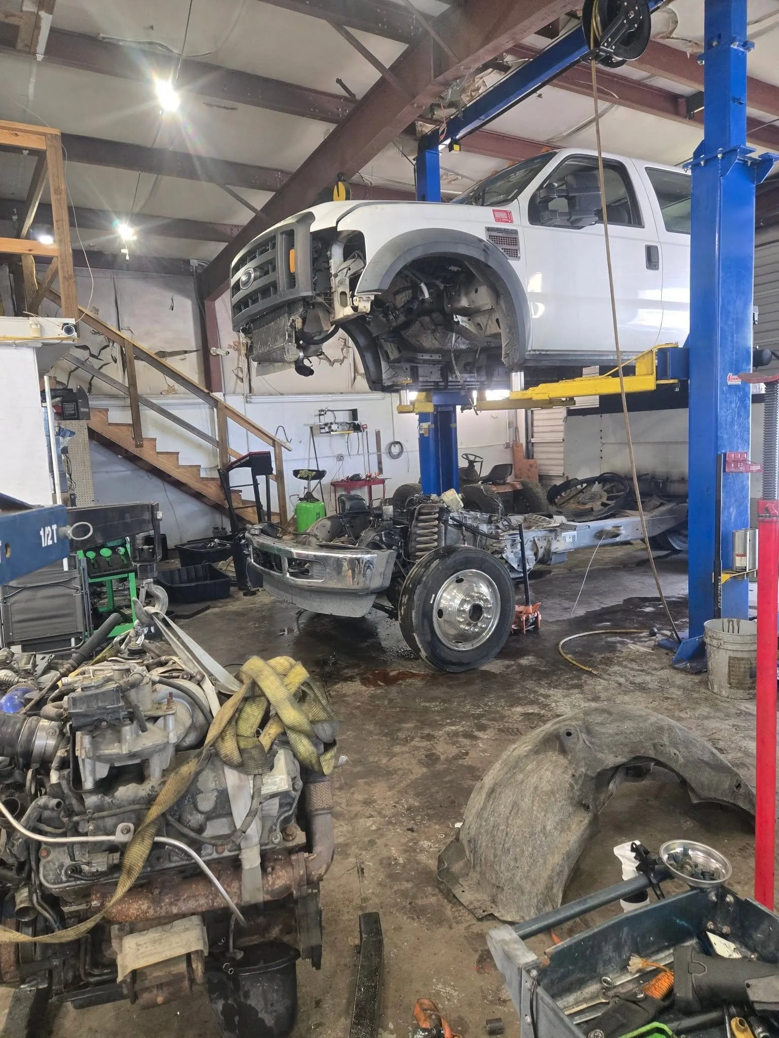 A Ford F-550 diesel truck raised on a lift at Riverside Automotive with its engine out for a major repair.