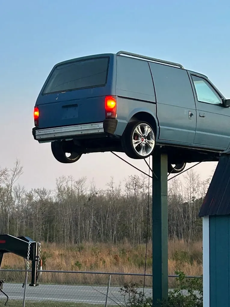 The blue minivan mounted on a pole that marks the Riverside Automotive location on Whiteville Road.