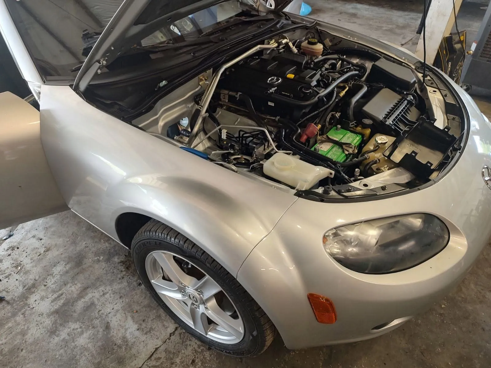A silver Mazda MX-5 Miata with the hood open at Riverside Automotive during maintenance service.