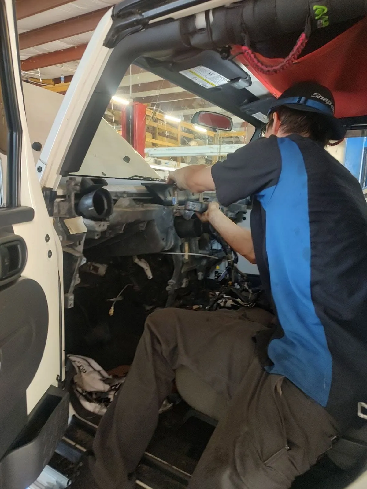 A Riverside Automotive technician working inside the dashboard of a Jeep on heating and A/C components.